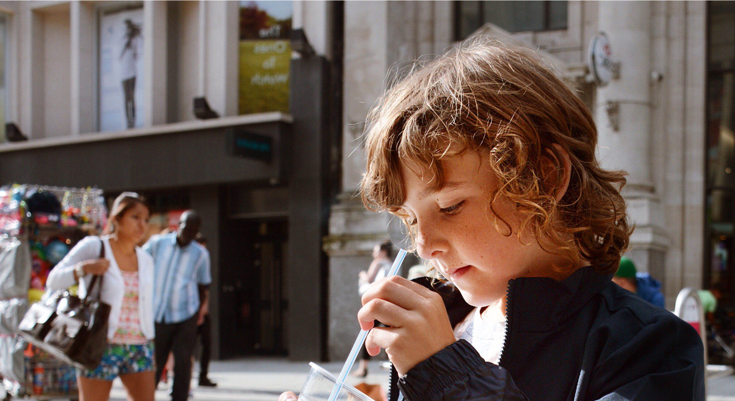 Long haired young boy in city centre with slush drink